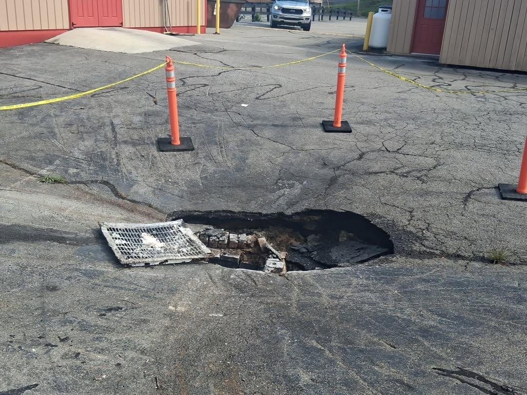 Collapsed catch basin in a commercial parking lot, grate displaced and asphalt caved in around it, area taped off