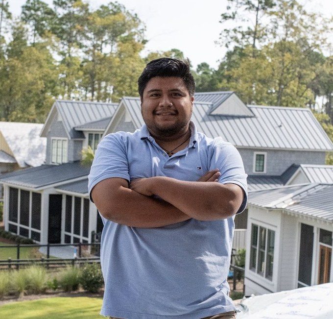 Cristian, Project Manager at D2R Builders, standing arms crossed in front of standing-seam metal roof homes