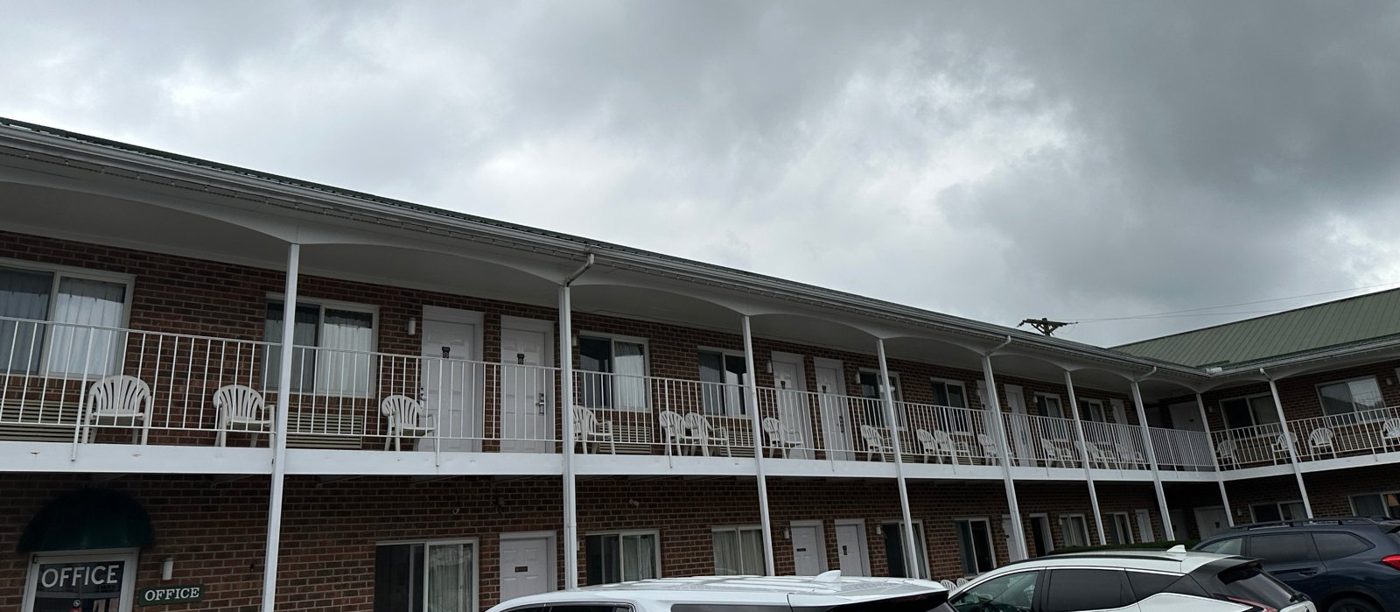 Two-story red brick inn with dated white railings and plastic chairs on the walkway