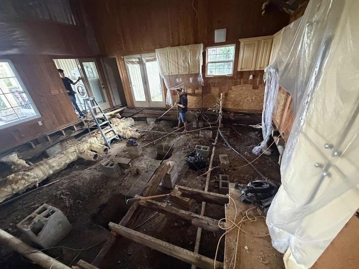 Kitchen floor removed down to the crawlspace, rotted joists and block piers exposed, D2R crew rebuilding the floor structure